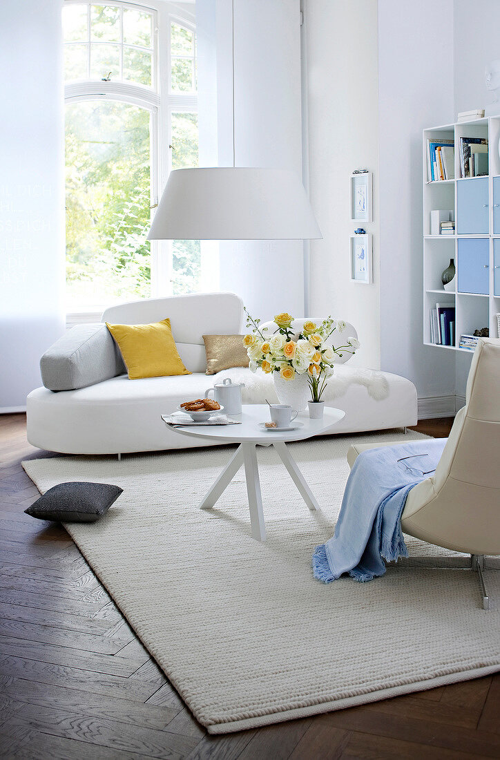 White sofa with yellow and golden cushions beside white coffee table with vase of flowers
