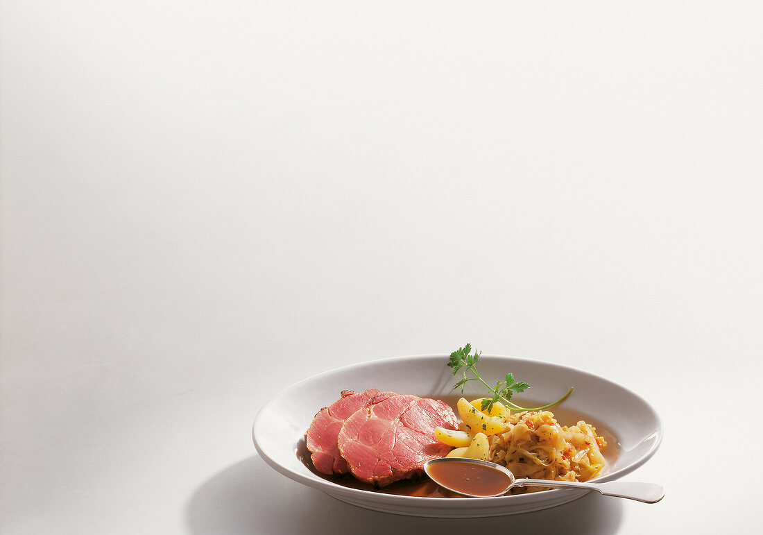 Plate of surbraten with sauerkraut, boiled potatoes and parsley on white background