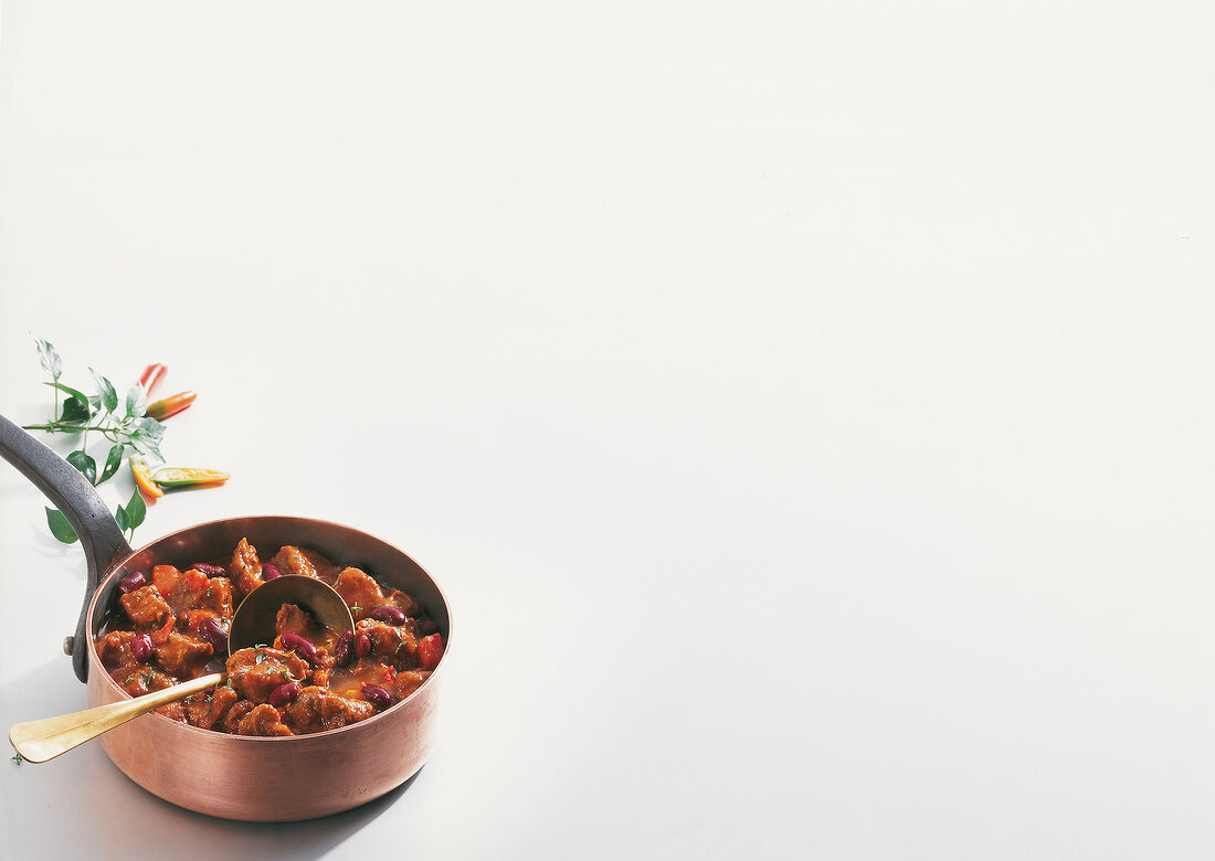 Lamb meat with chilli and kidney beans in pot on white background, copy space
