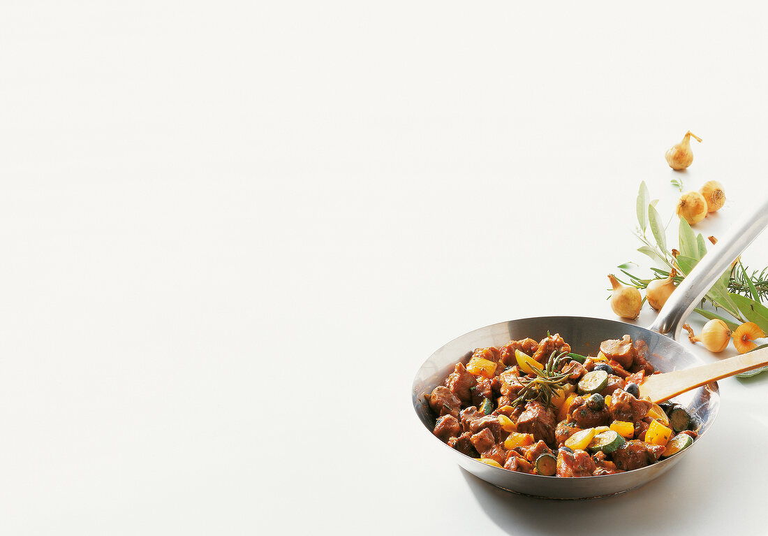 Lamb ragout with peppers and zucchini in pan on white background