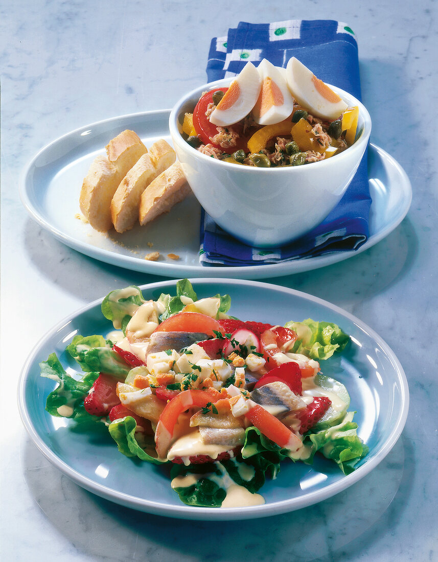 Tuna salad with egg in bowl and herring salad with strawberries on plate