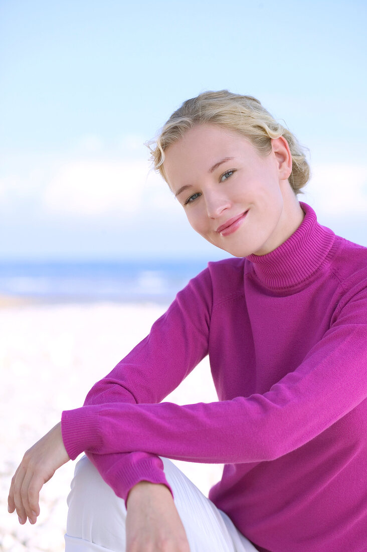 Portrait of pretty blonde woman wearing pink turtleneck sweater on the beach, smiling