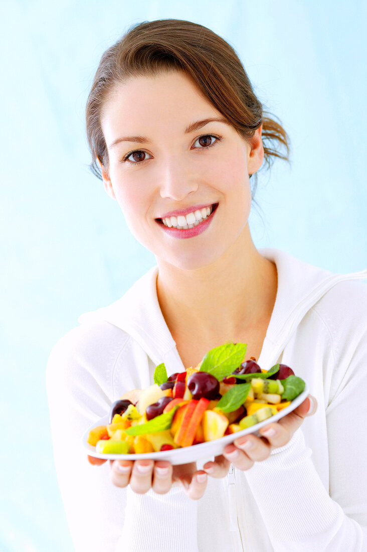 Portrait of beautiful woman holding plate of fresh fruits in hand