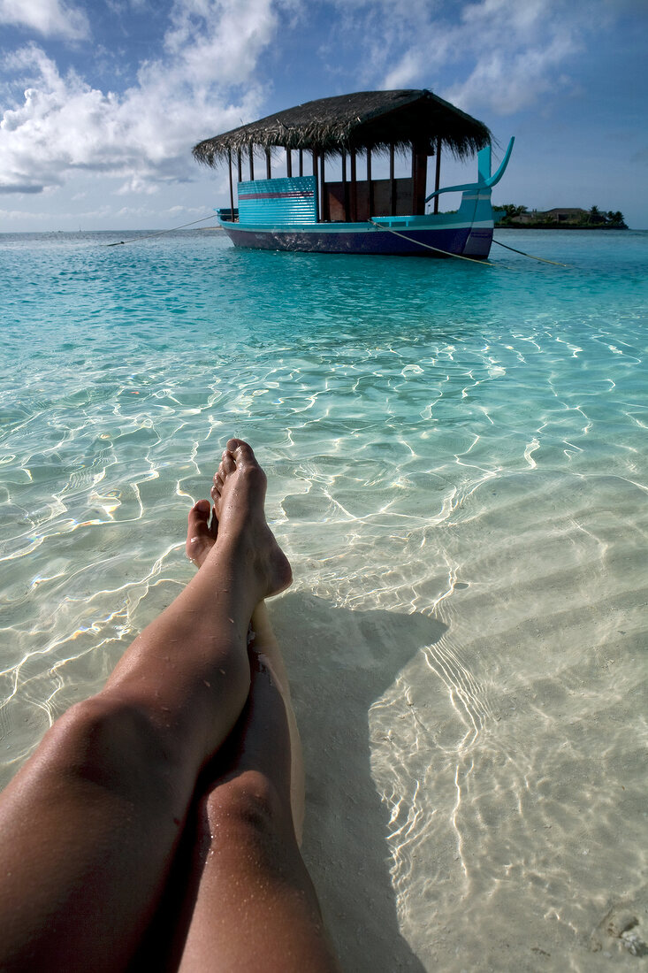 Close-up of legs in shallow water and boat in Veliganduhuraa island, Maldives
