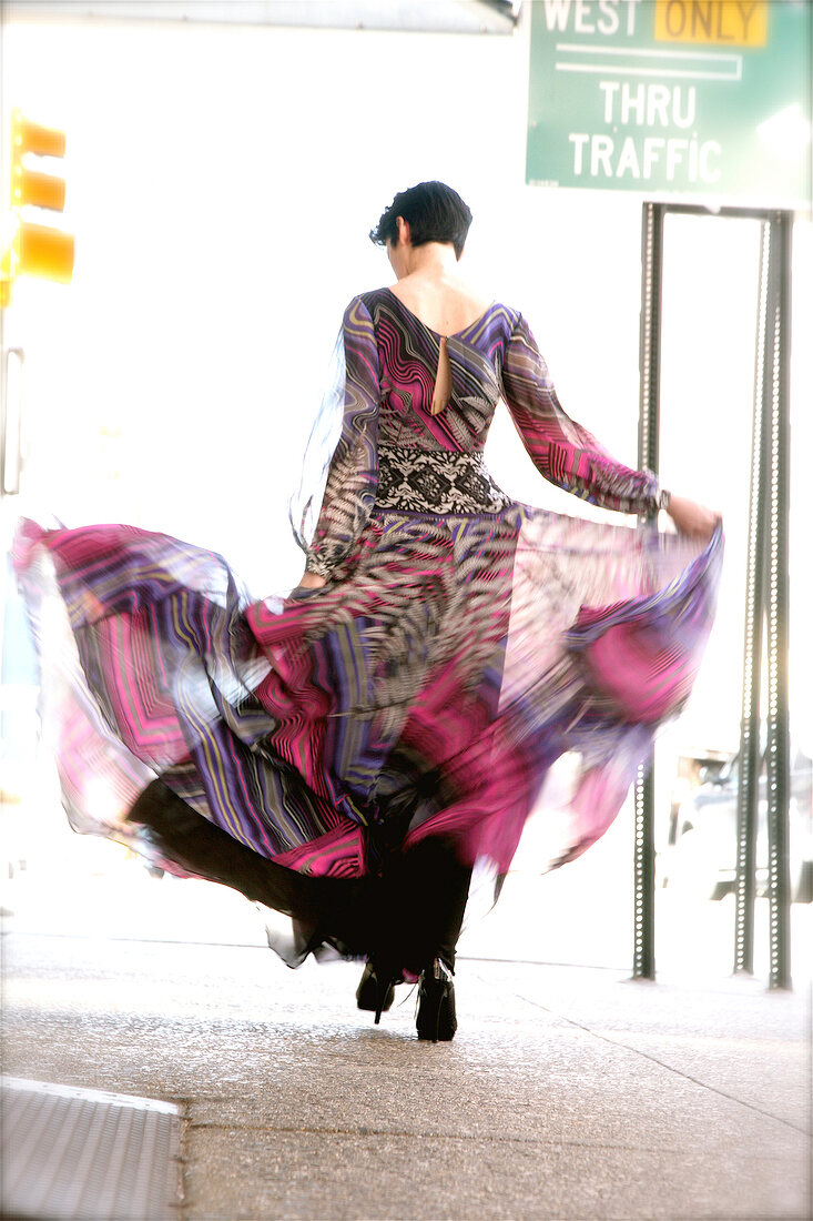 Rear view of woman swinging her dress while walking on the street
