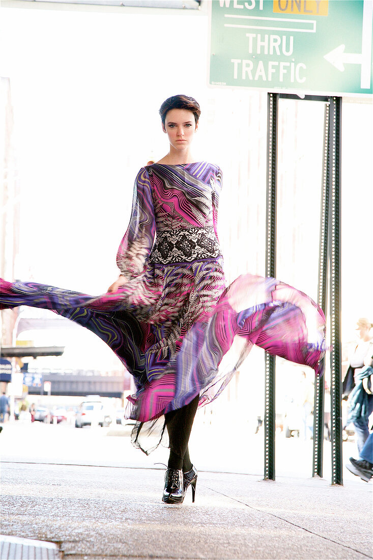 Portrait of serious looking woman swinging her dress while walking on the road