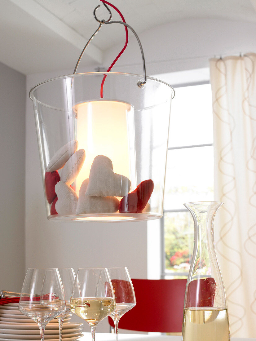 Suspension lamp filled with fabric hearts hanging above table with wine glasses