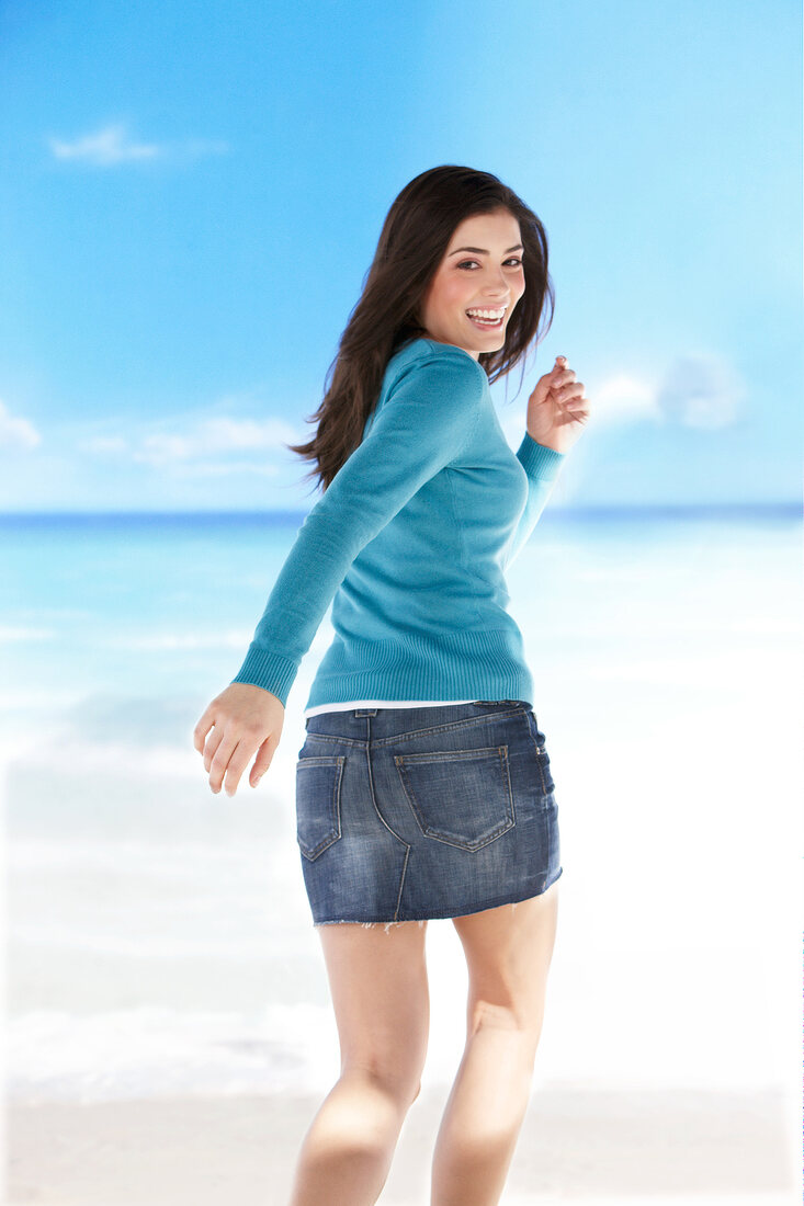 Pretty woman in blue sweater running on beach, smiling while looking over shoulder