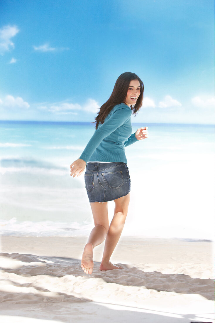 Frau läuft am Strand in Jeansrock und blauem Pulli