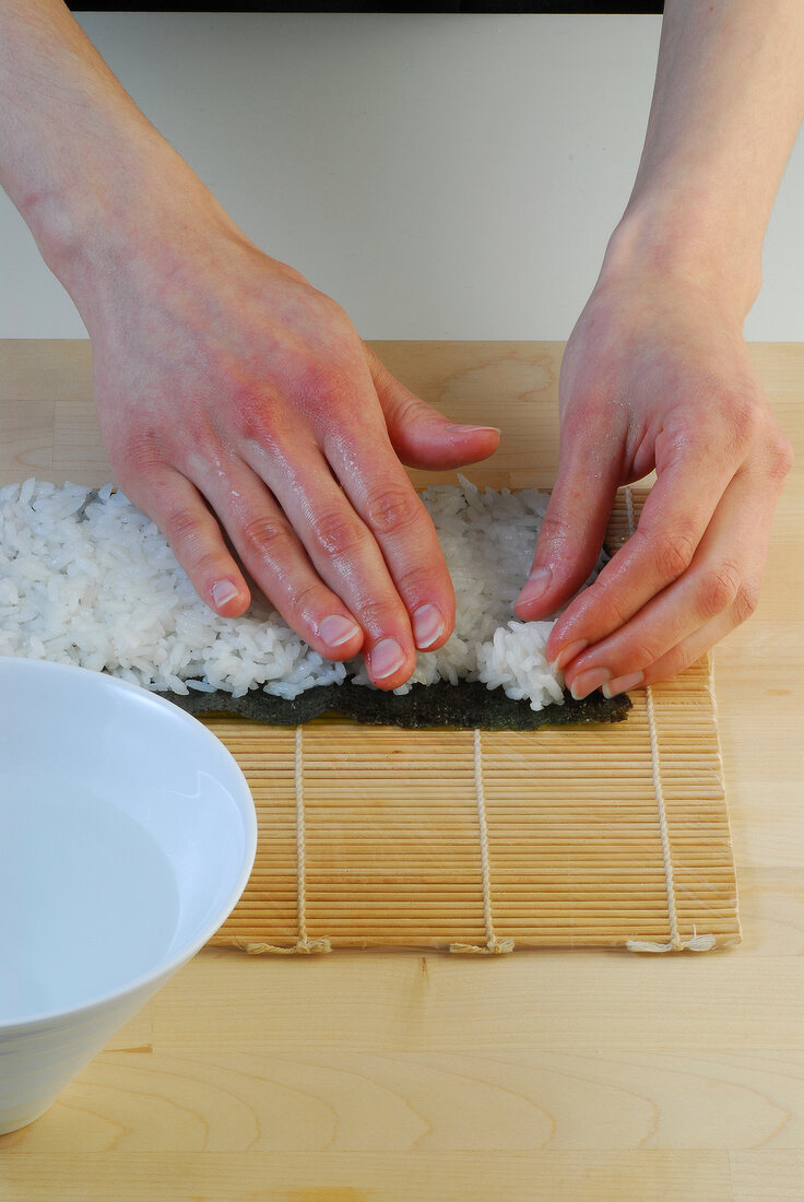 Rice being spread on nori sheet for preparation of sushi on sushi mat, step 1