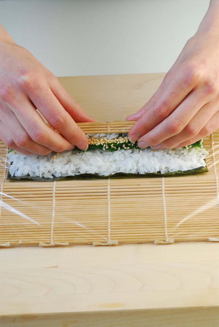 Sushi mat with nori sheet and rice being rolled while preparing sushi, step 3