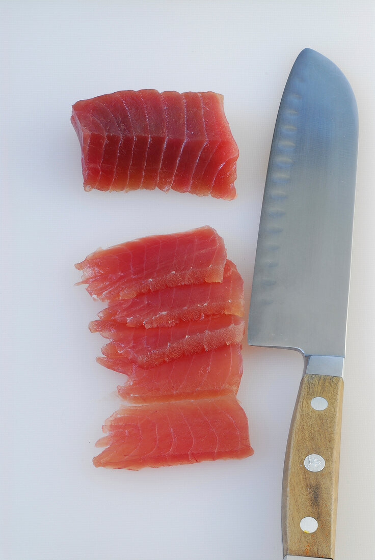 Slices of tuna with knife on white background, step 1