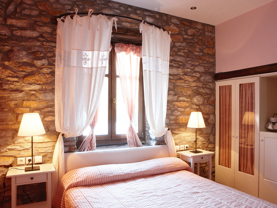 View of Mediterranean style room with bed, side tables and natural stone walls in Greece