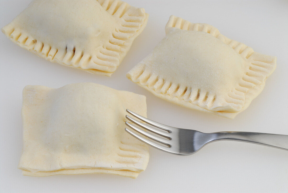 Edges of stuffed dough being pressed by fork while preparing puff, step 3