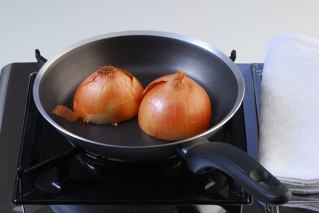 Halved onion being fried on pan while preparing chicken broth, step 4