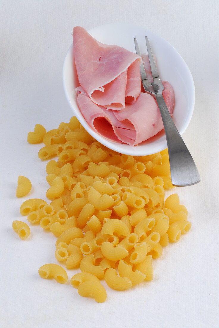 Raw ham in bowl and elbow pasta on white background