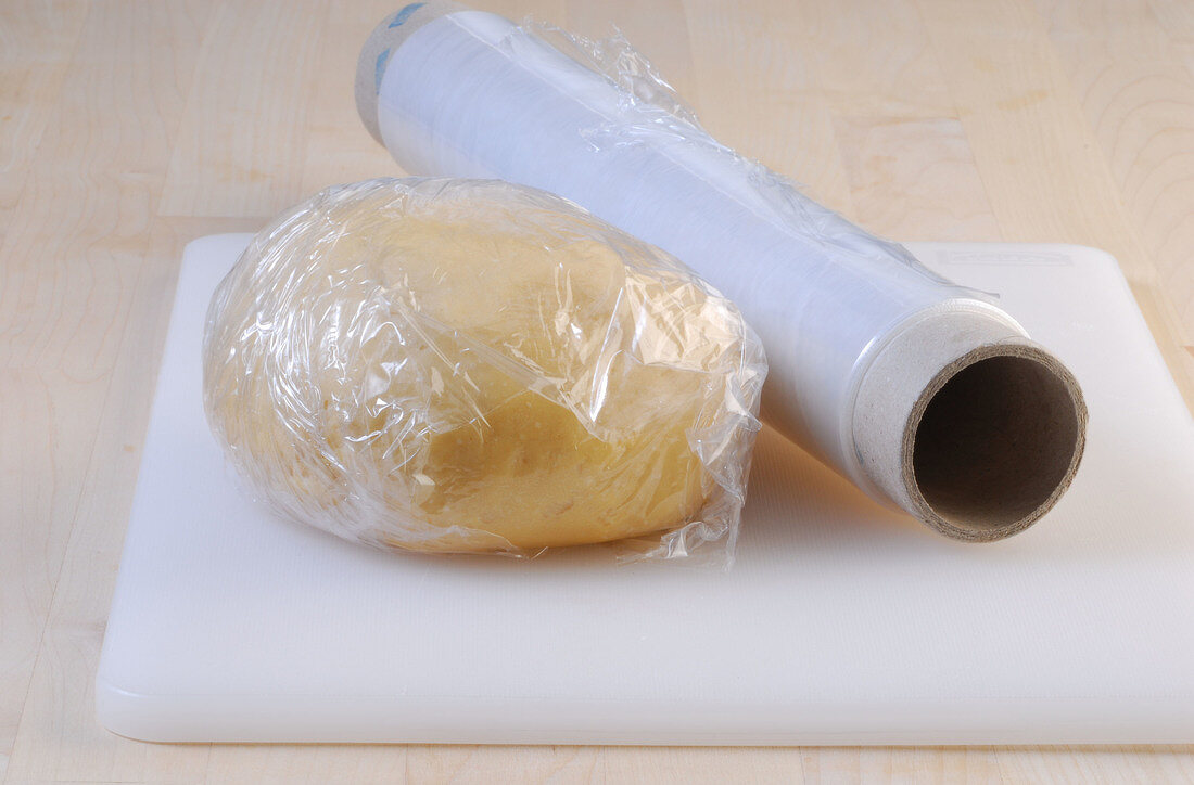 Dough wrapped in plastic foil on cutting board while preparing noodles, step 2