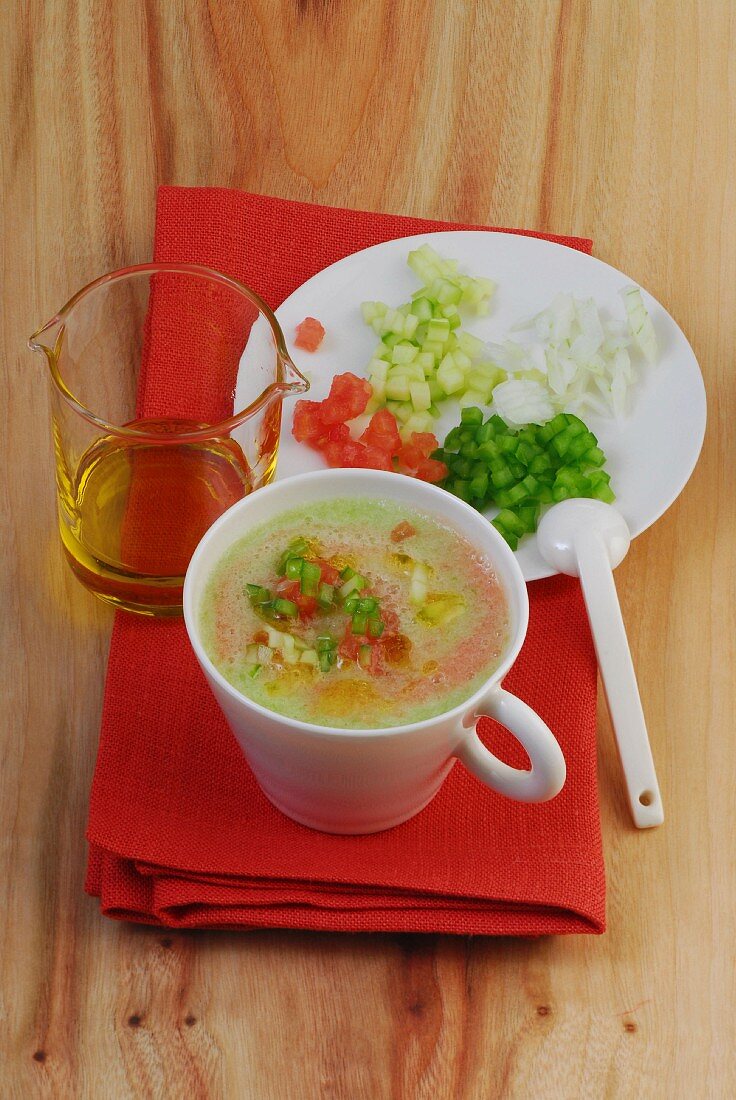 A cup of gazpacho with a plate of diced vegetables next to it