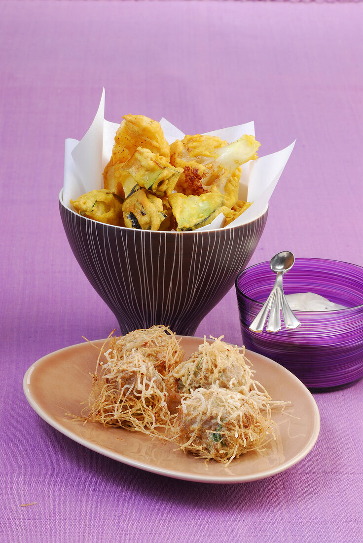 Fried vegetables in bowl and meatballs covered with noodles on plate