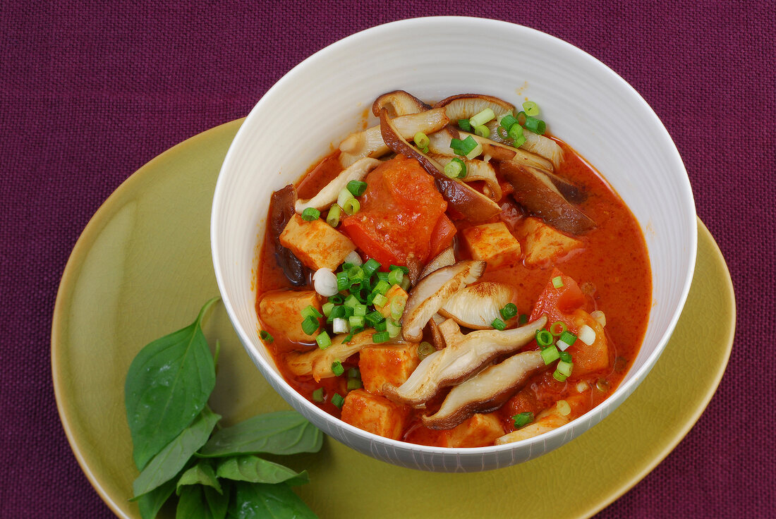 Red tofu curry with shiitake mushrooms, tomatoes and herbs in bowl
