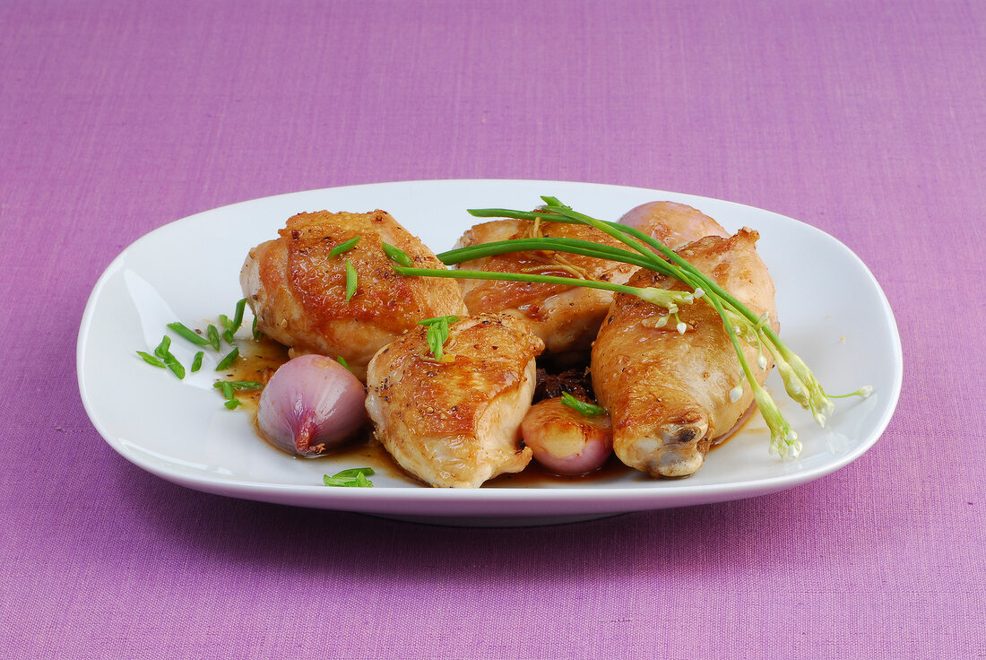 Braised chicken with shallots and garlic garnished with chives on plate