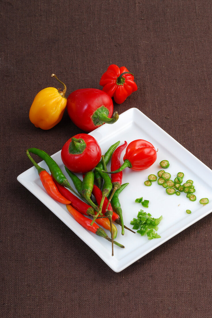 Plate of various chillies and peppers on brown background