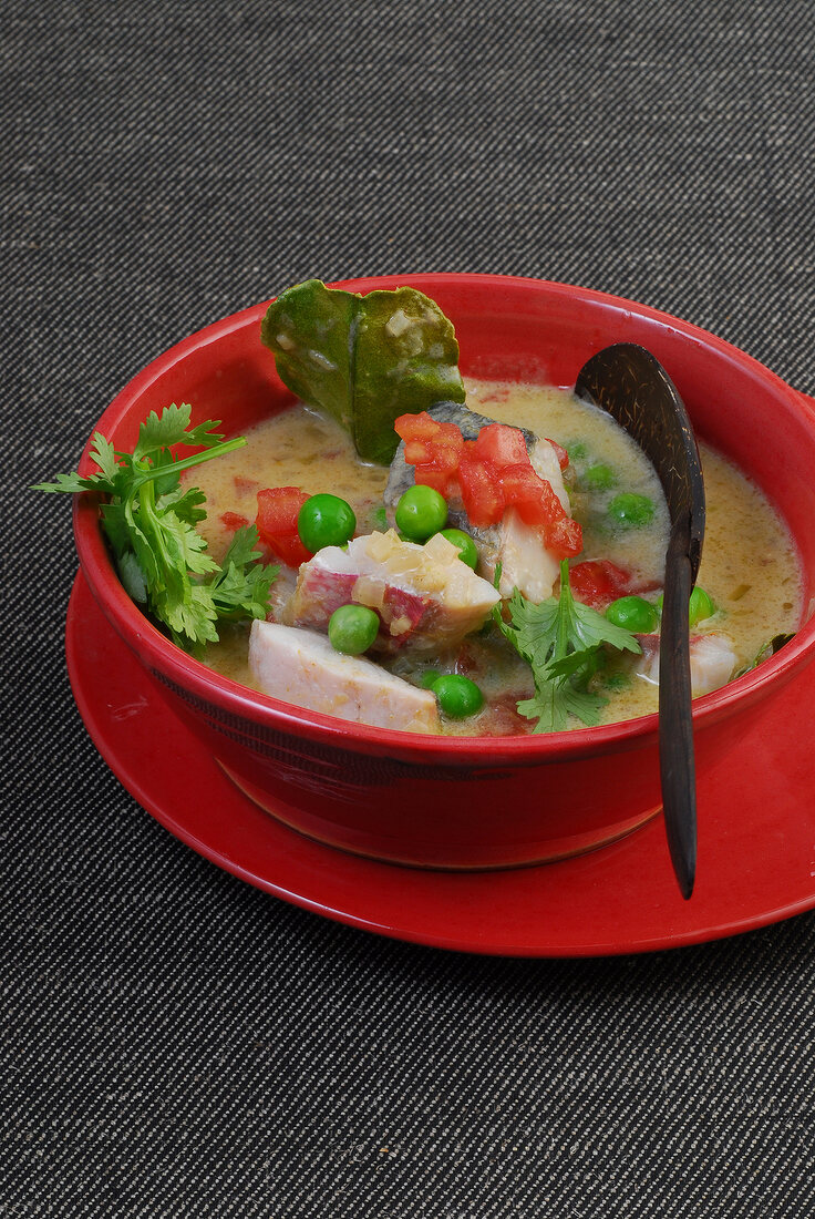 Fish curry with tomatoes, peas, onions and coconut milk in bowl