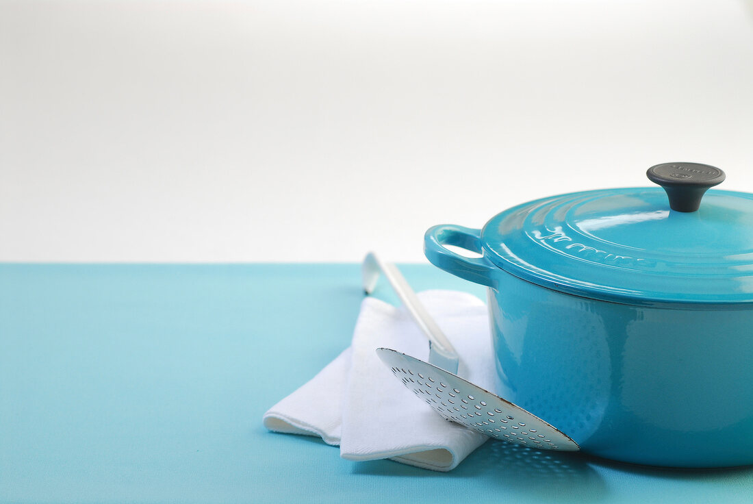 Blue roasting pot with ladle and kitchen towel on blue background