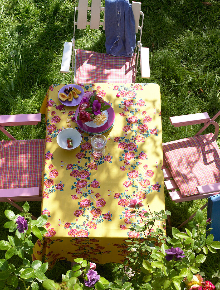 Table and chairs with floral patterned tablecloth in garden, overhead view