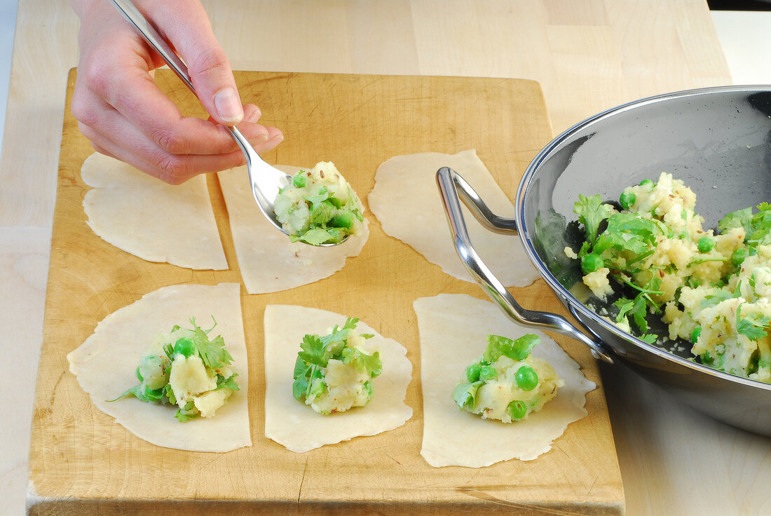 Potatoes and peas stuffing being put on dough sheet while preparing samosas, step 4