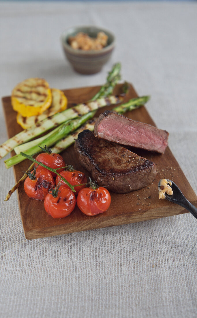 Steak with grilled vegetables, asparagus and cherry tomatoes on wooden board