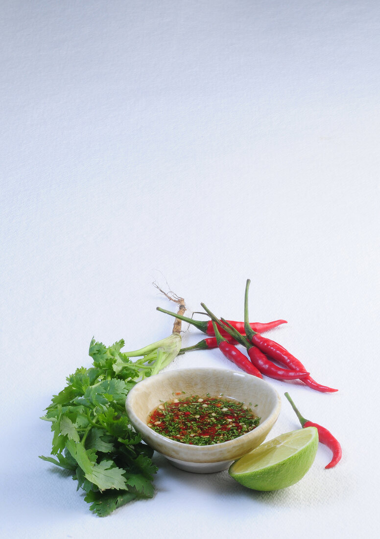 Bowl of lime and chilli sauce with red chilli peppers and lemon wedge on white background