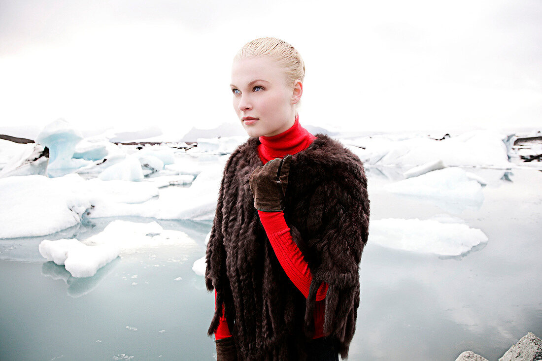 Contemplative blonde woman wearing fur poncho standing near floes and looking away