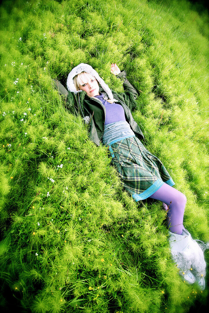 Fashionable woman wearing plaid skirt and purple pantyhose lying on the grass