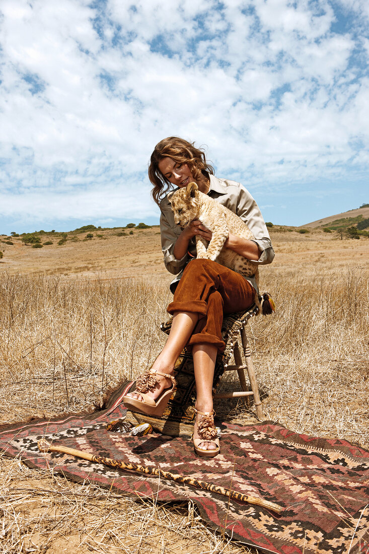 Woman holding lion cub and sitting on stool in steppe