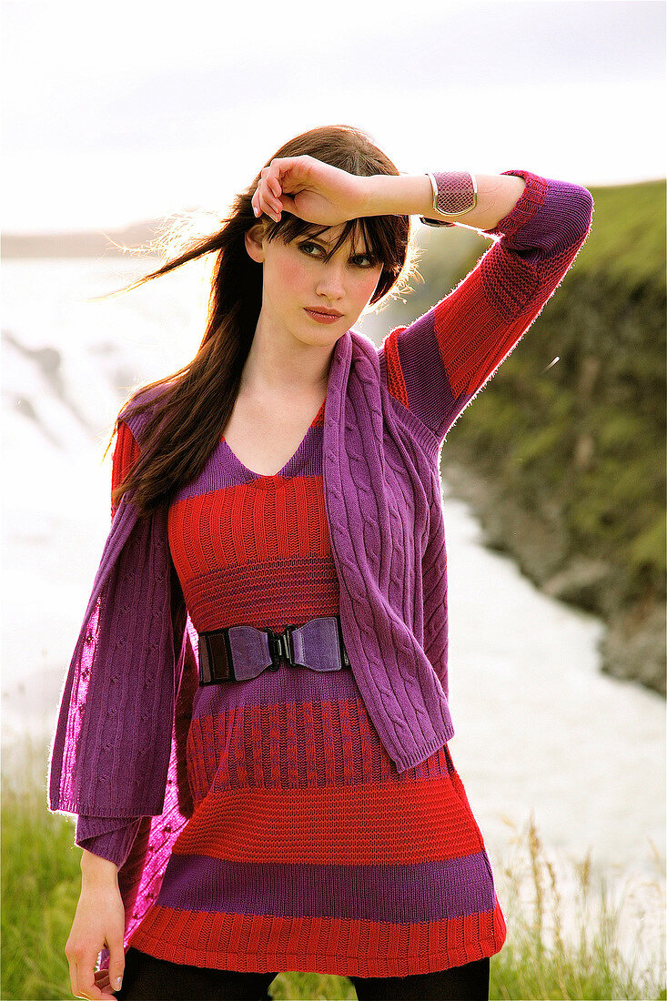 Fashionable woman with brown hair wearing purple sweater, standing in front of waterfall