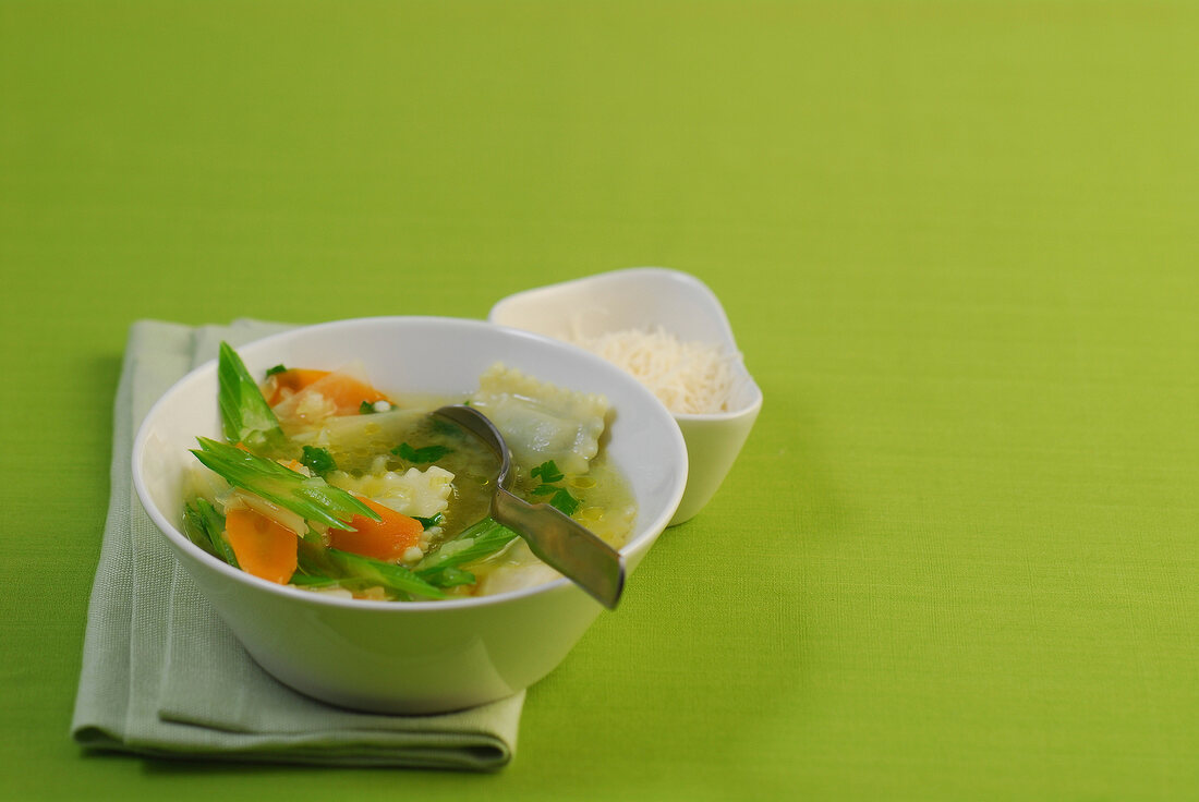 Bowl of ravioli with vegetable stew on green background