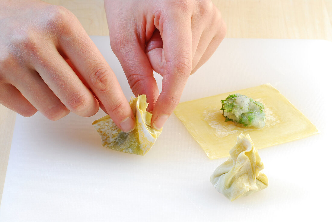 Stuffed dough sheet being squeezed like bag while preparing wontons, step 4