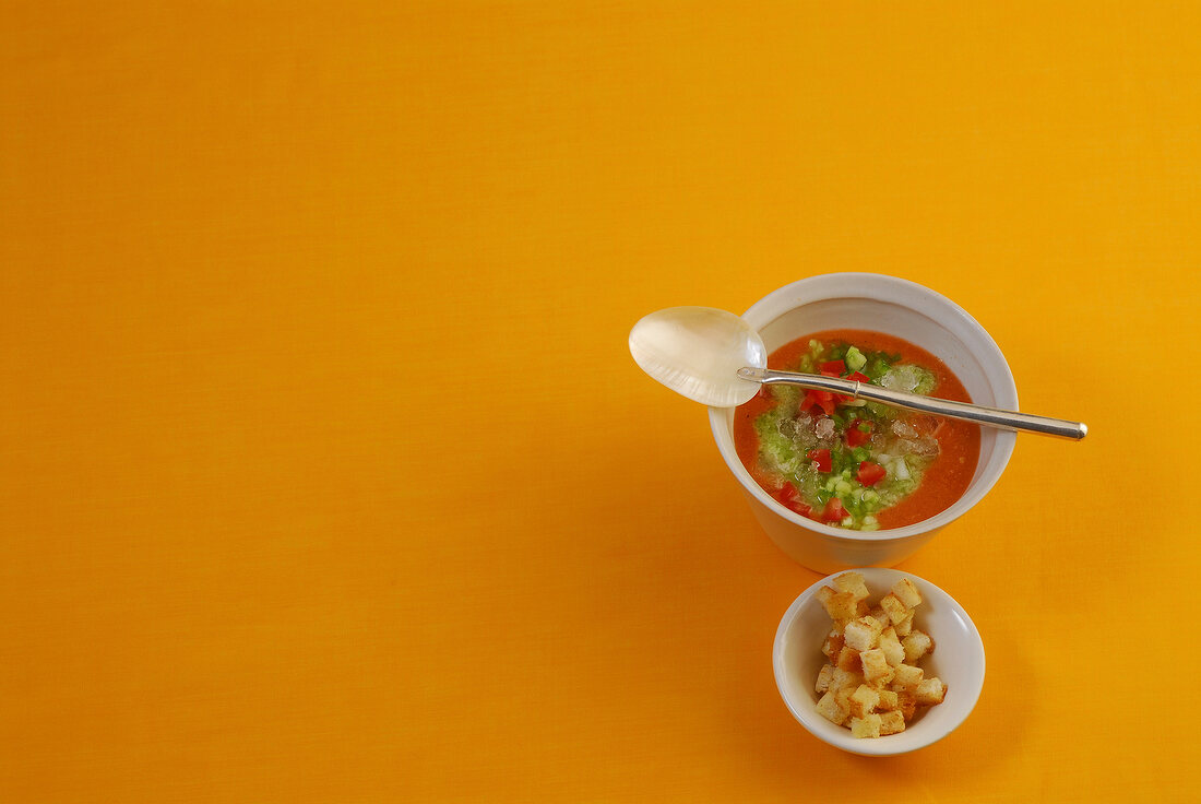 Bowl of cold tomato and cucumber soup with spoon, overhead view