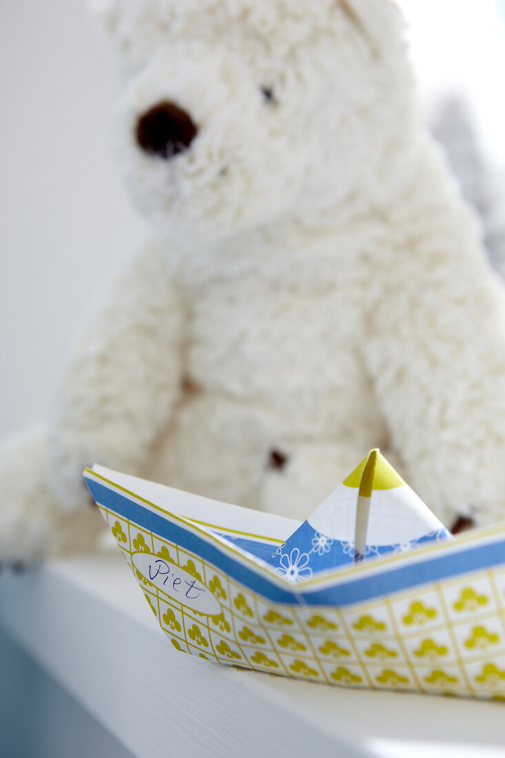 Teddy bear and paper boat on white background