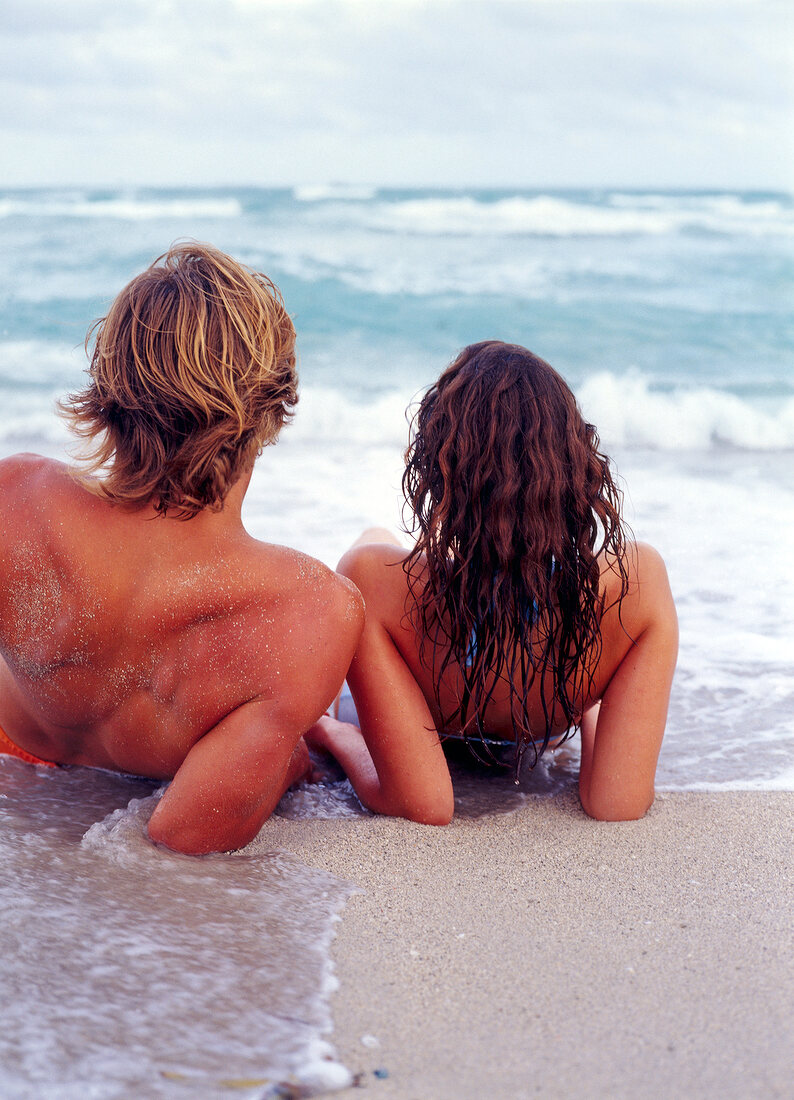 Mann und Frau liegen im Wasser am Strand, blicken aufs Meer.