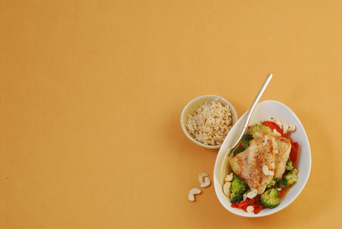 Bowls of fish with broccoli and brown rice on beige background
