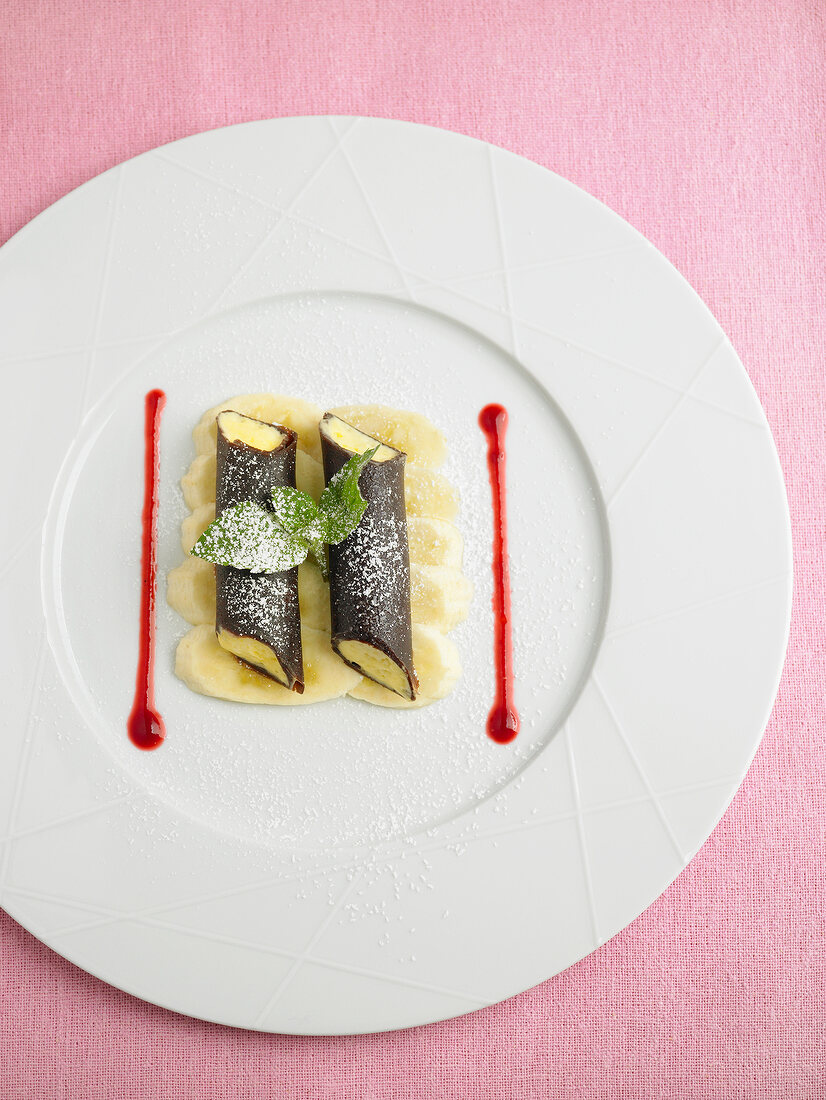 Cannelloni chocolate pancake garnished with mango mousse and sugar on plate