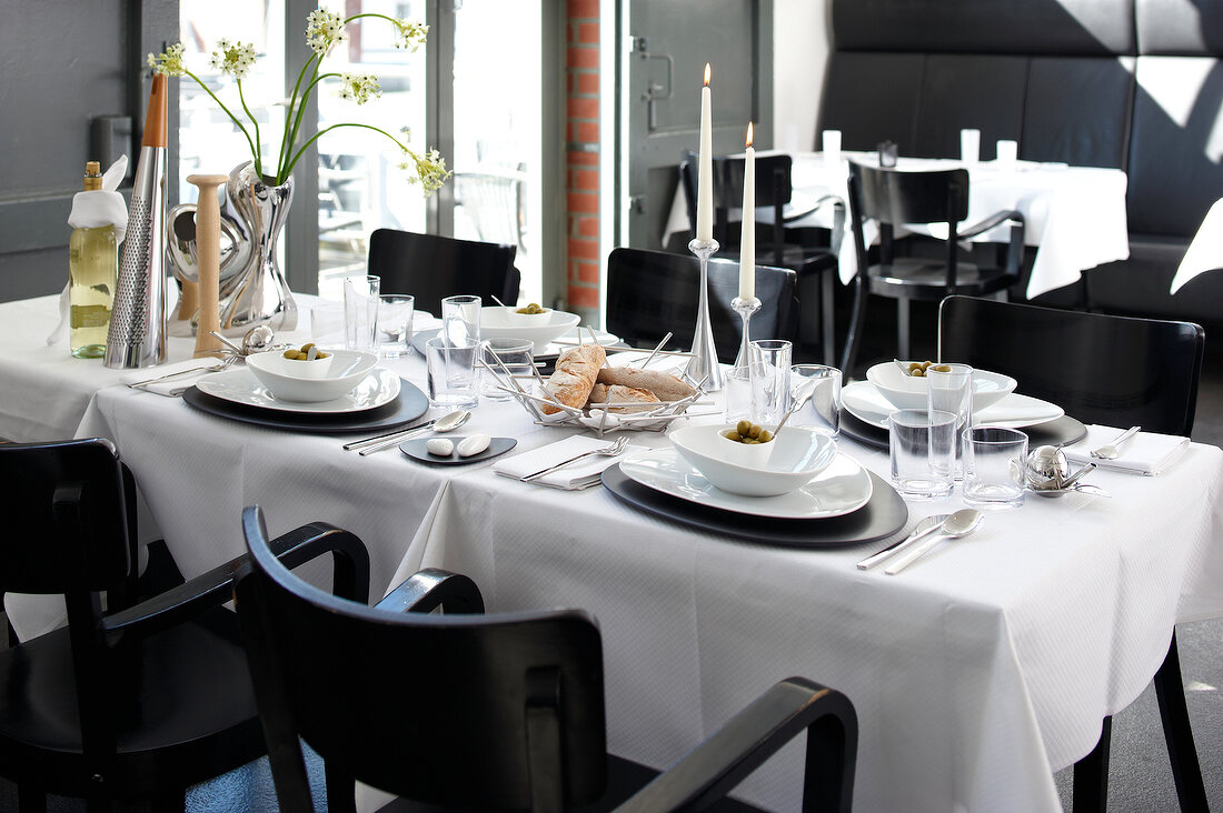 Table with black and white setting with white bread and olives