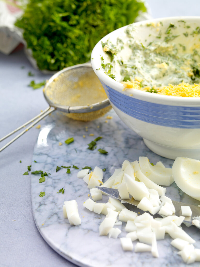 Green sauce with herbs in bowl, eggs and sieve on board