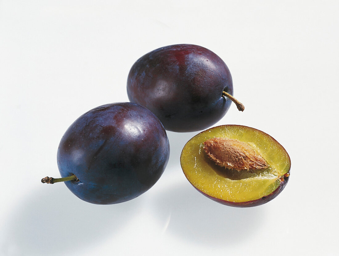 Two whole and halved blue plums on white background