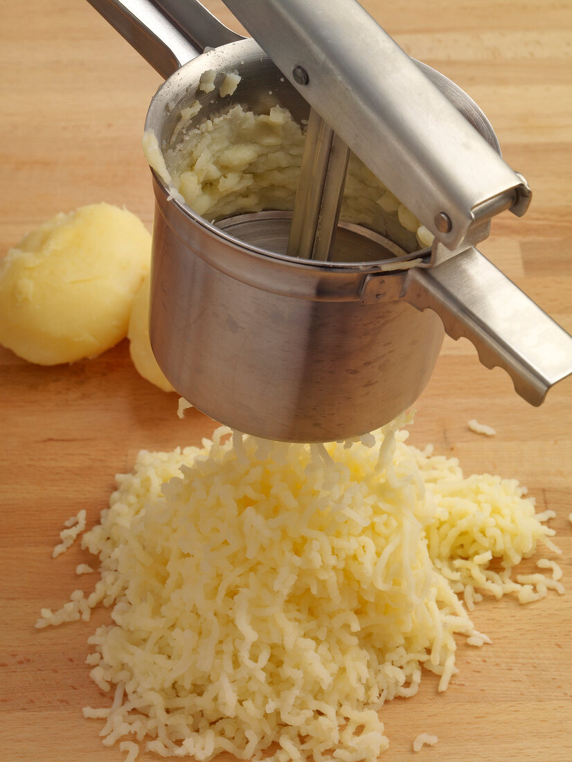 Close-up of potatoes being press in machine while preparing potato noodles, step 1