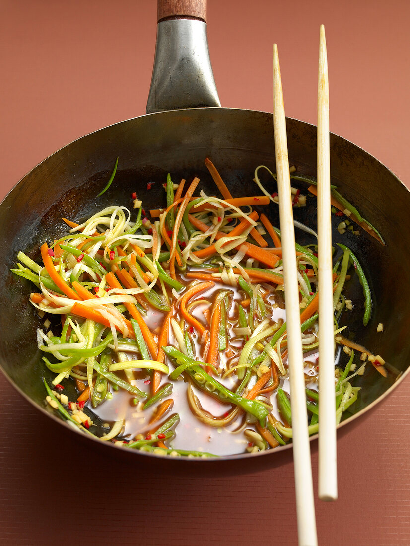 Sweet and sour vegetable sauce with carrot and leek in frying pan with chopsticks