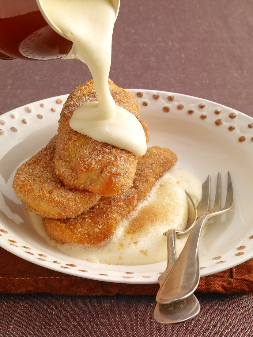 Wine cream sauce being poured on toast with sugar in serving dish