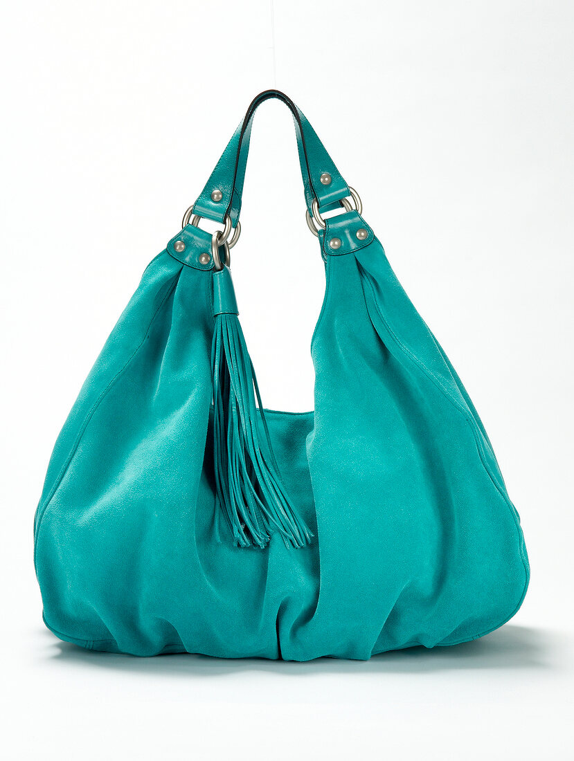 Close-up of turquoise suede handbag with tassel on white background